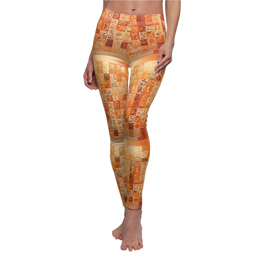 A pair of skinny fit leggings with geometric patterns in orange, creams, and browns with black and cream calligraphy on a female model.